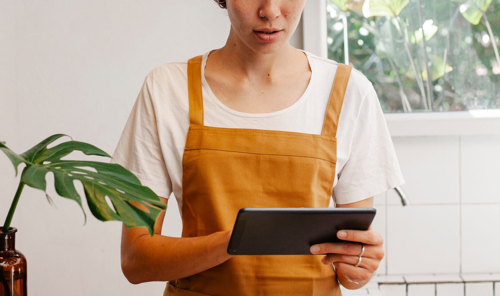 Profesional de cafetería revisando una tablet de pie junto a una ventana con luz natural